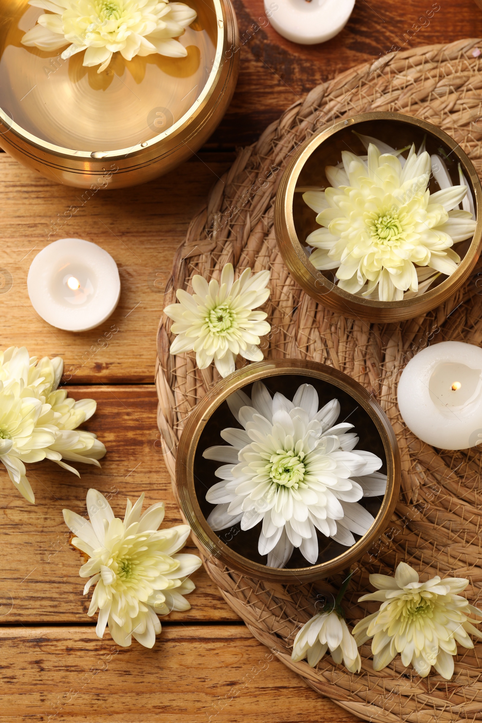 Photo of Tibetan singing bowls, beautiful chrysanthemum flowers and burning candles on wooden table, flat lay