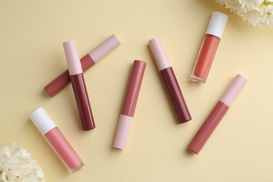 Photo of Different lip glosses and flowers on pale yellow background, flat lay