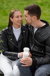 Lovely young couple with cups of coffee on bench outdoors. Romantic date