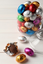 Photo of Glass jar with chocolate eggs wrapped in colorful foil on white wooden table