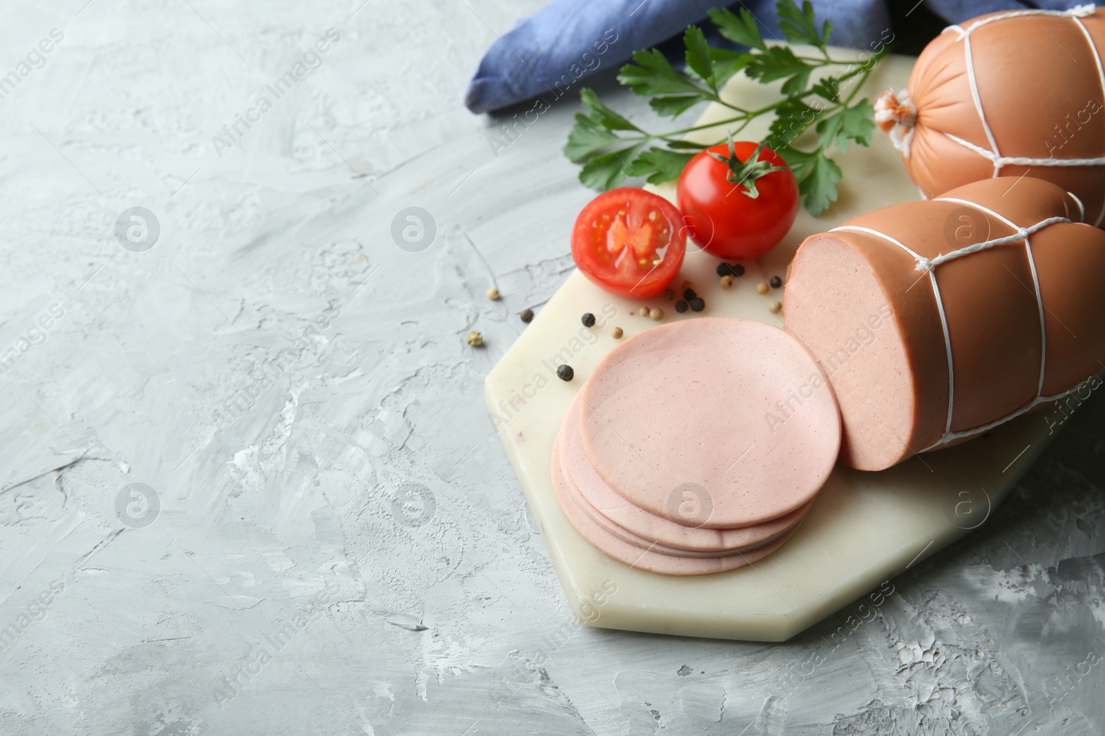 Photo of Delicious boiled sausage with tomatoes, parsley and spices on grey textured table. Space for text