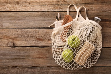 Photo of Net bag with different items on wooden table, top view and space for text. Conscious consumption