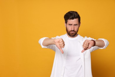 Handsome bearded man showing thumbs down on orange background. Space for text
