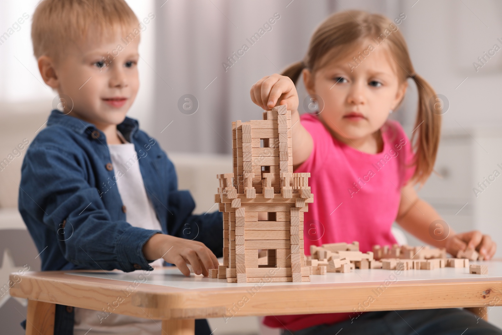 Photo of Little girl and boy playing with wooden tower at table indoors, selective focus. Children's toy