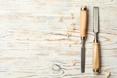 Photo of Chisels and shavings on white wooden background, flat lay with space for text. Carpenter's tools