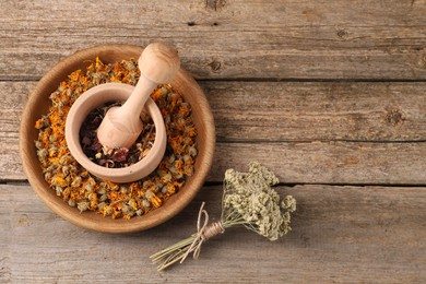 Photo of Mortar with pestle, many different dry herbs and flowers on wooden table, flat lay. Space for text