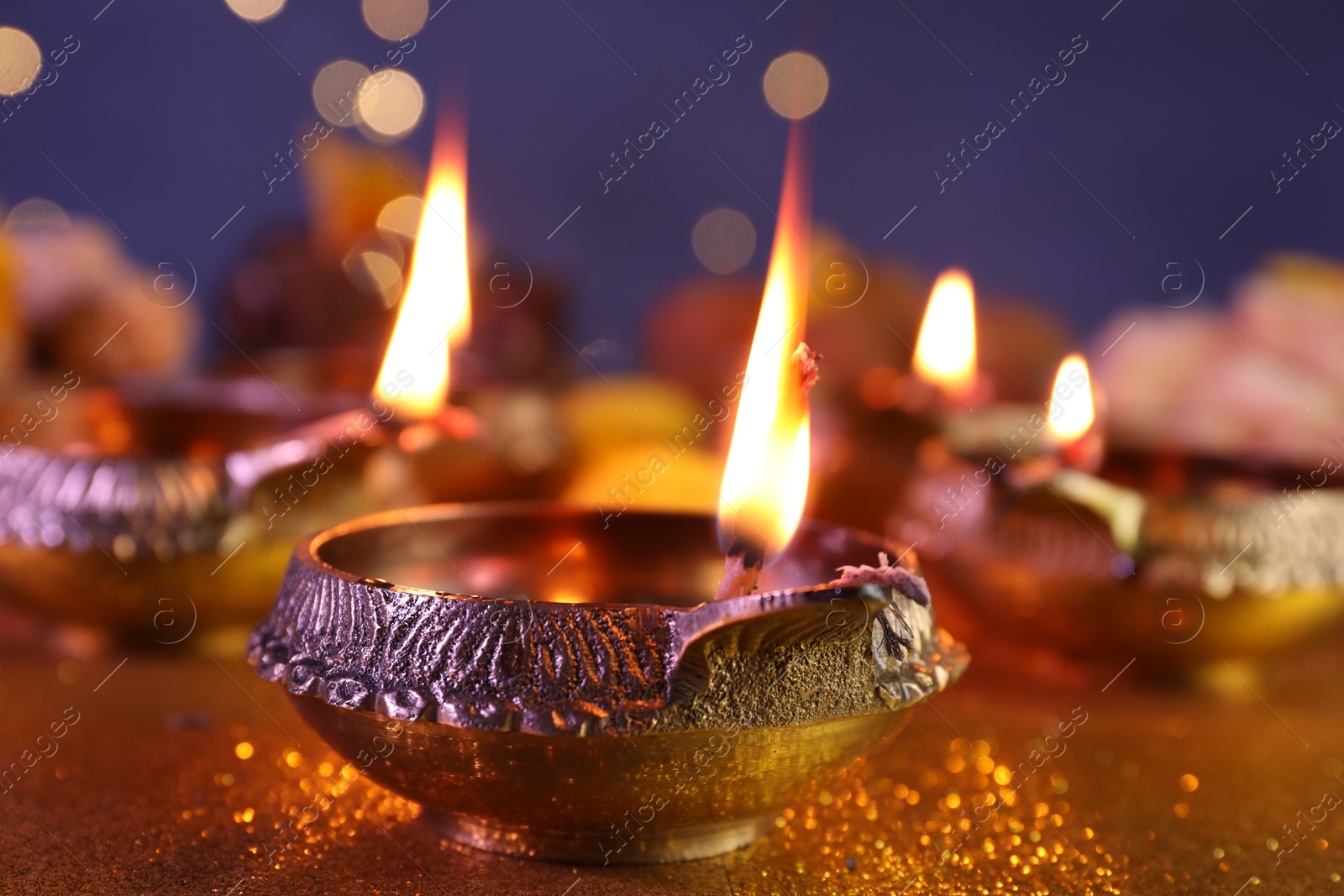 Photo of Diwali celebration. Diya lamp on shiny golden table against blurred lights, closeup