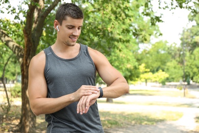 Photo of Young man checking pulse with smartwatch after training outdoors