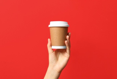 Woman holding takeaway paper coffee cup on red background, closeup