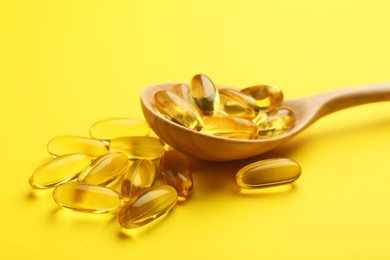 Photo of Vitamin capsules in wooden spoon on yellow background, closeup