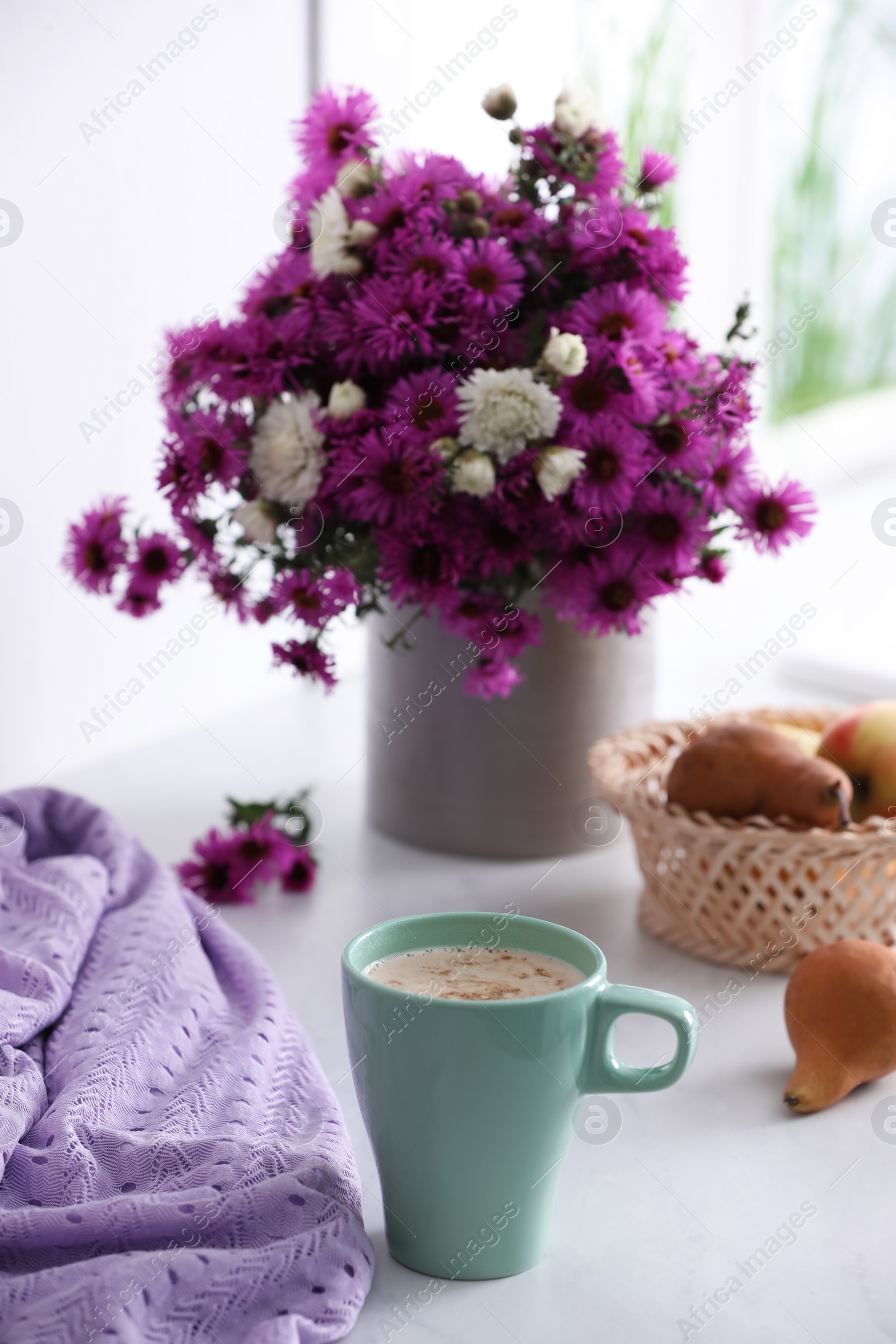 Photo of Cup of aromatic coffee, beautiful flowers and violet cloth on white table