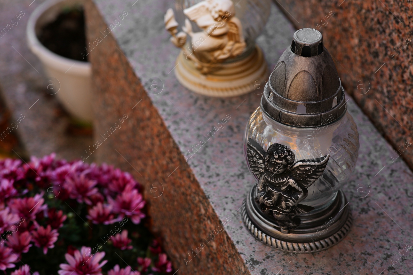 Photo of Grave lanterns and flowers on granite surface in cemetery