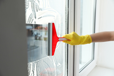 Photo of Woman cleaning window with squeegee indoors, closeup