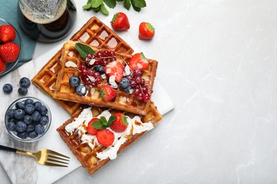 Photo of Board with delicious Belgian waffles, berries and whipped cream on light marble table, flat lay. Space for text