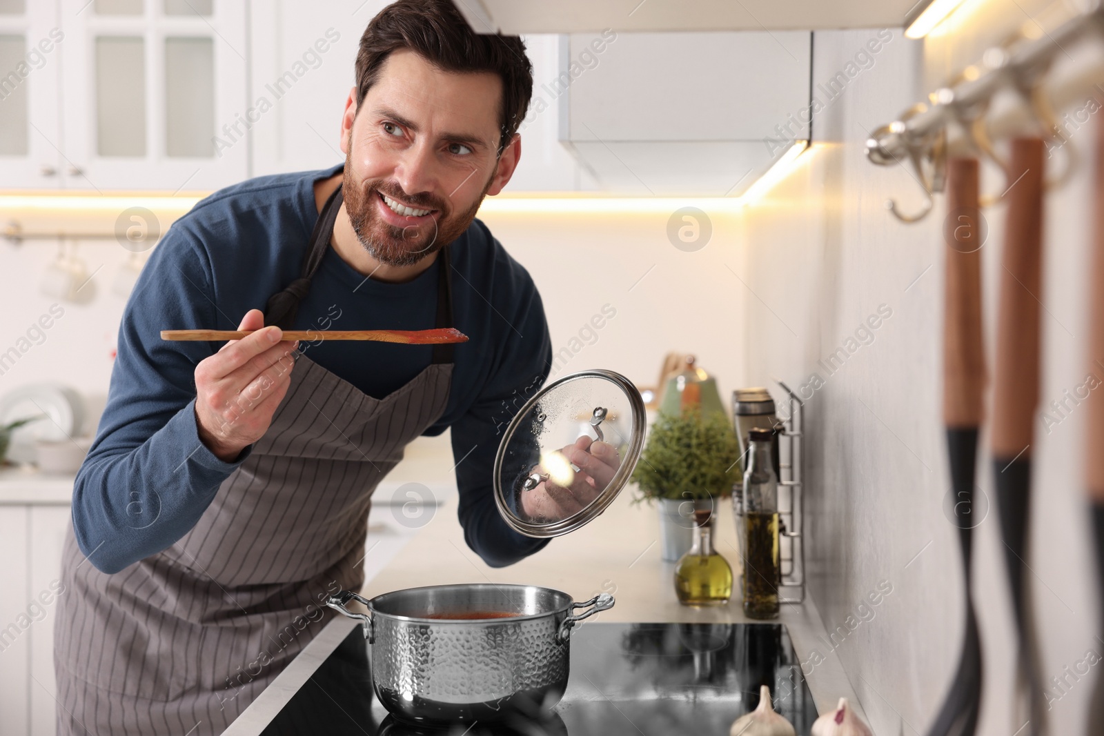 Photo of Man cooking tomato soup on cooktop in kitchen