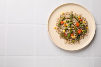 Delicious pearl barley with vegetables on white tiled table, top view. Space for text