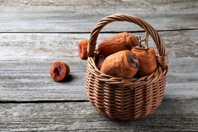 Wicker basket with tasty dried persimmon fruits on wooden table, space for text