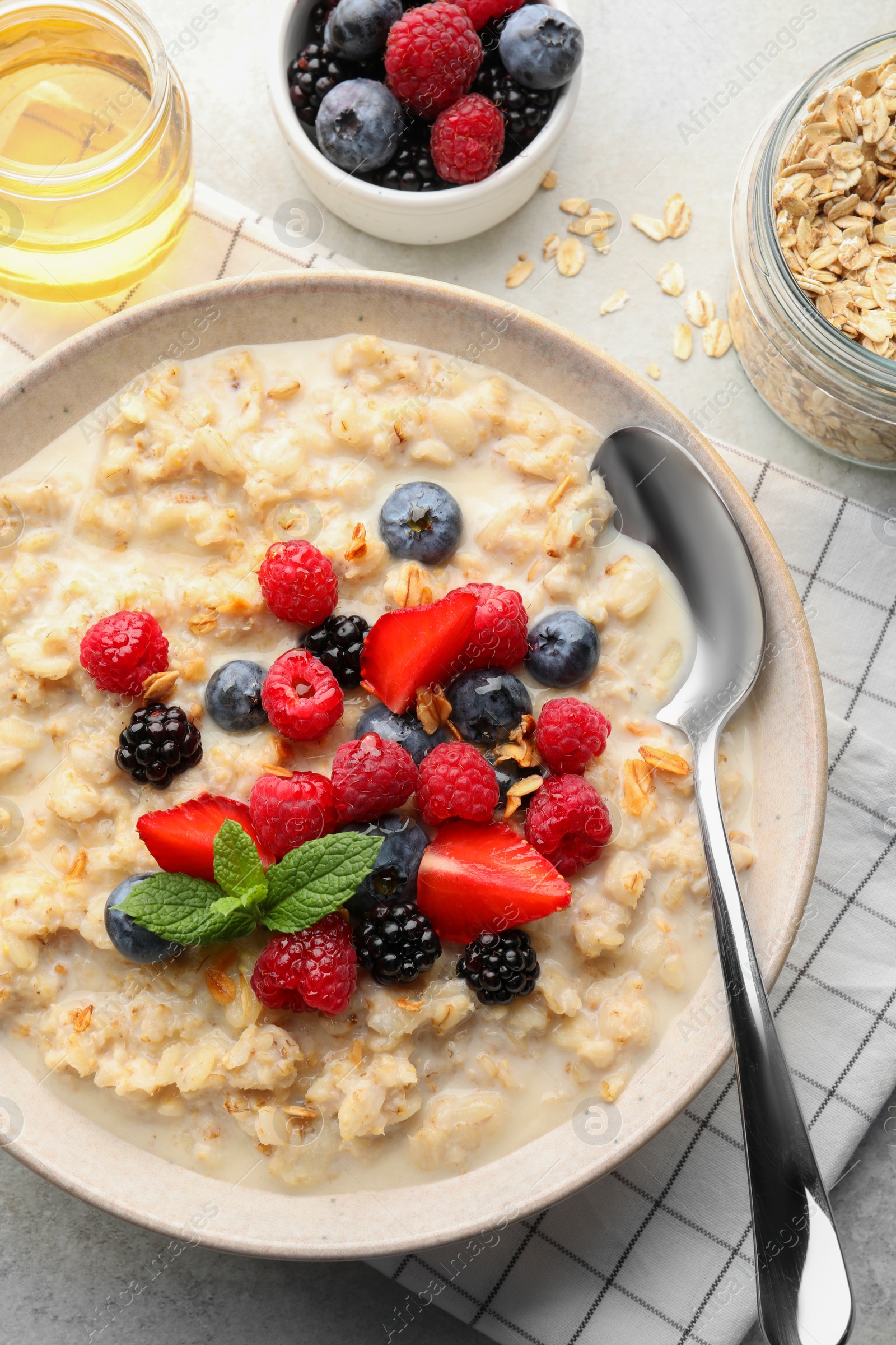 Photo of Bowl of oatmeal porridge served with berries on light grey table, flat lay