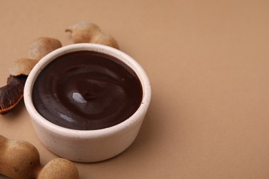 Photo of Bowl of tamarind sauce and fresh pods on light brown table. Space for text