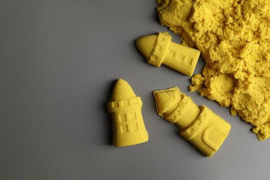 Photo of Castle figures made of yellow kinetic sand on grey background, flat lay. Space for text