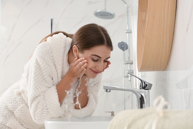 Young woman washing her face with water in bathroom