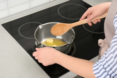 Woman stirring butter in saucepan on electric stove, closeup