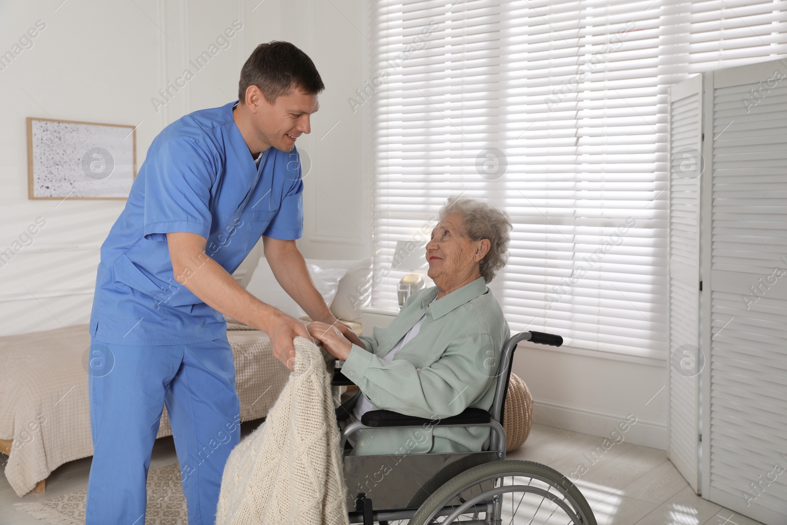 Photo of Caregiver assisting senior woman in wheelchair indoors. Home health care service