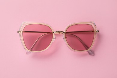 Photo of New stylish sunglasses on pink background, top view