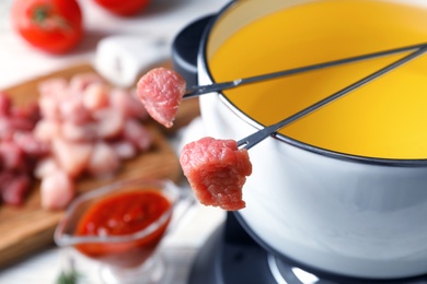 Photo of Fondue pot and forks with raw meat on table, closeup