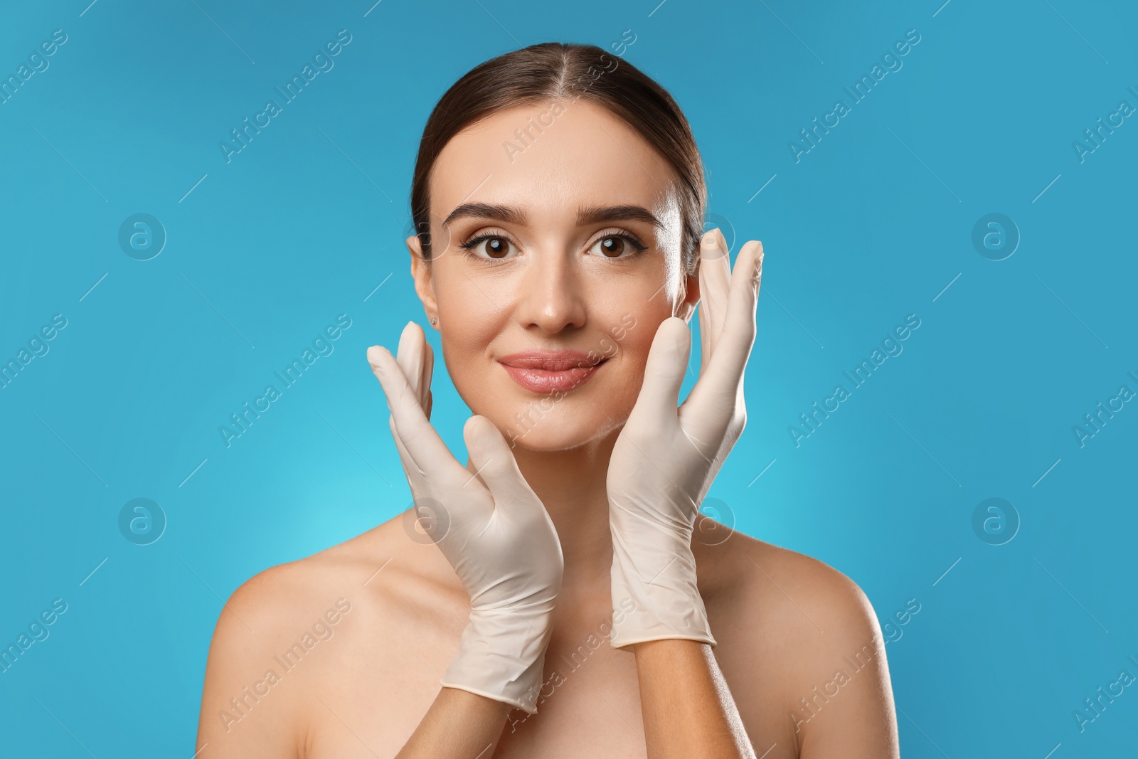 Photo of Doctor examining woman's face before plastic surgery on light blue background
