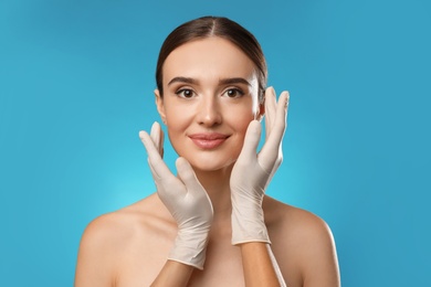 Doctor examining woman's face before plastic surgery on light blue background