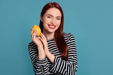 Photo of Happy woman with red dyed hair holding whole lemon on light blue background