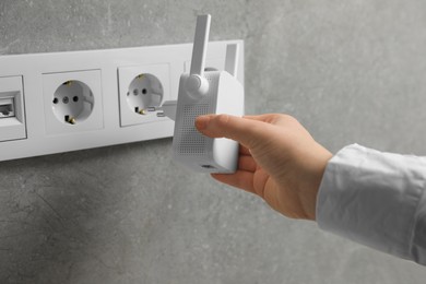 Woman inserting wireless Wi-Fi repeater into power socket indoors, closeup