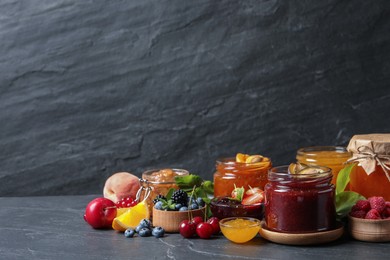 Photo of Jars with different jams and fresh fruits on black table. Space for text