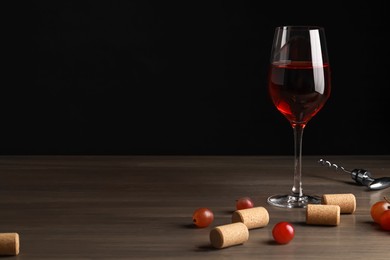 Photo of Glass of red wine, corks and corkscrew on wooden table. Space for text