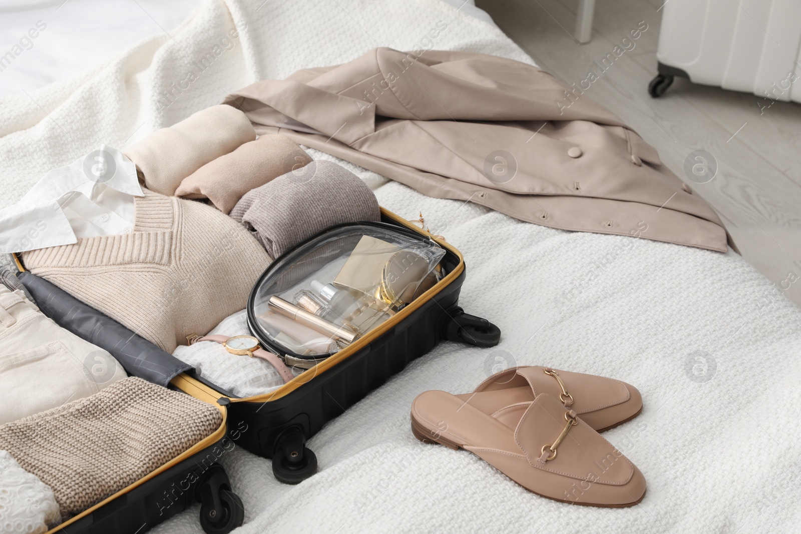 Photo of Open suitcase with folded clothes, shoes and accessories on bed in room