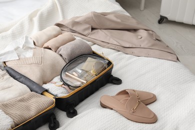 Open suitcase with folded clothes, shoes and accessories on bed in room