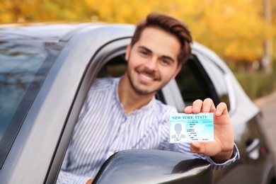 Photo of Young man holding driving license in car