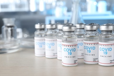 Glass vials with COVID-19 vaccine on wooden table. Space for text