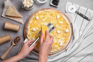 Woman grating cheese onto homemade pizza on table, top view