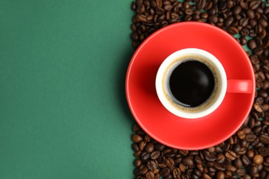 Cup of hot aromatic espresso and roasted beans on green background, flat lay. Space for text