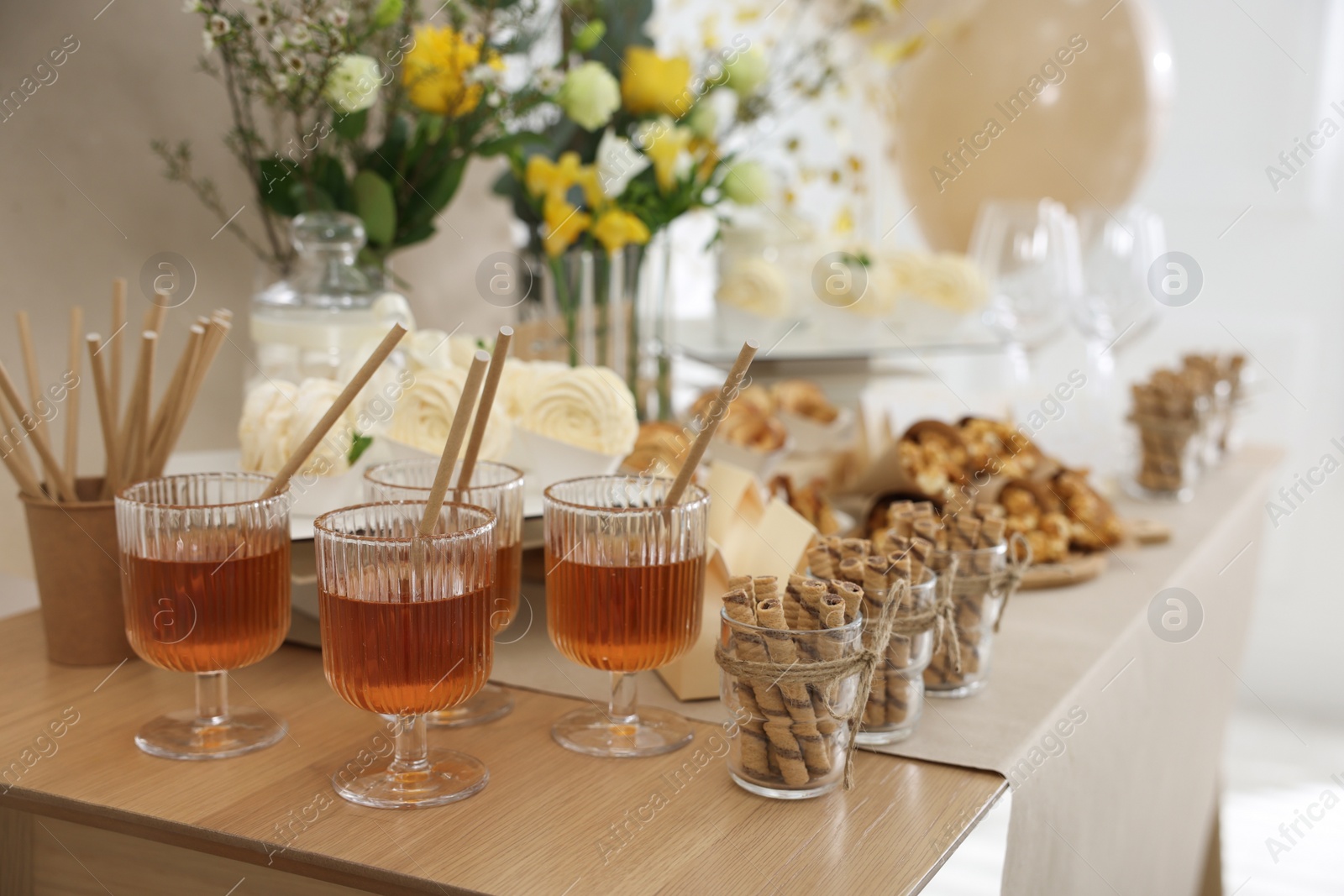 Photo of Tasty treats and glasses of drink on table in room. Sweet buffet