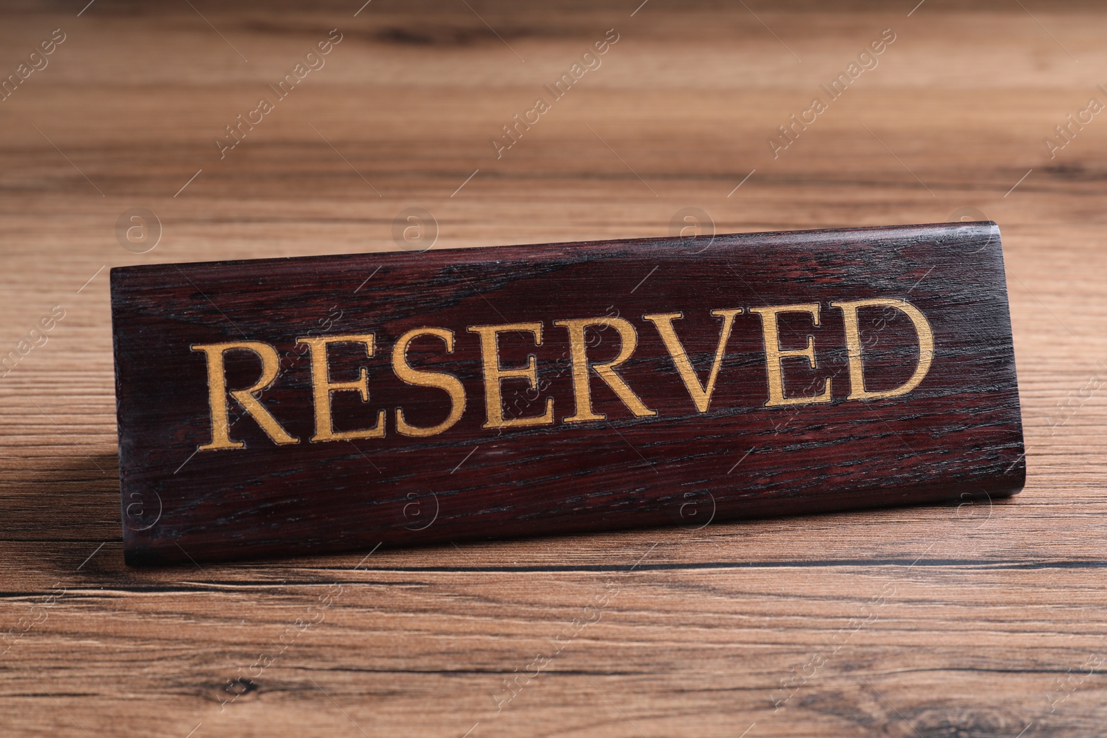 Photo of Elegant sign RESERVED on wooden surface. Table setting element