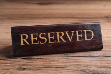Photo of Elegant sign RESERVED on wooden surface. Table setting element