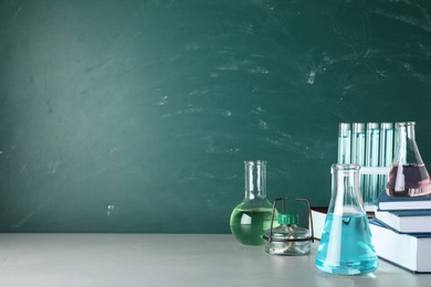 Laboratory equipment and books on table near chalkboard with space for text. Chemistry concept