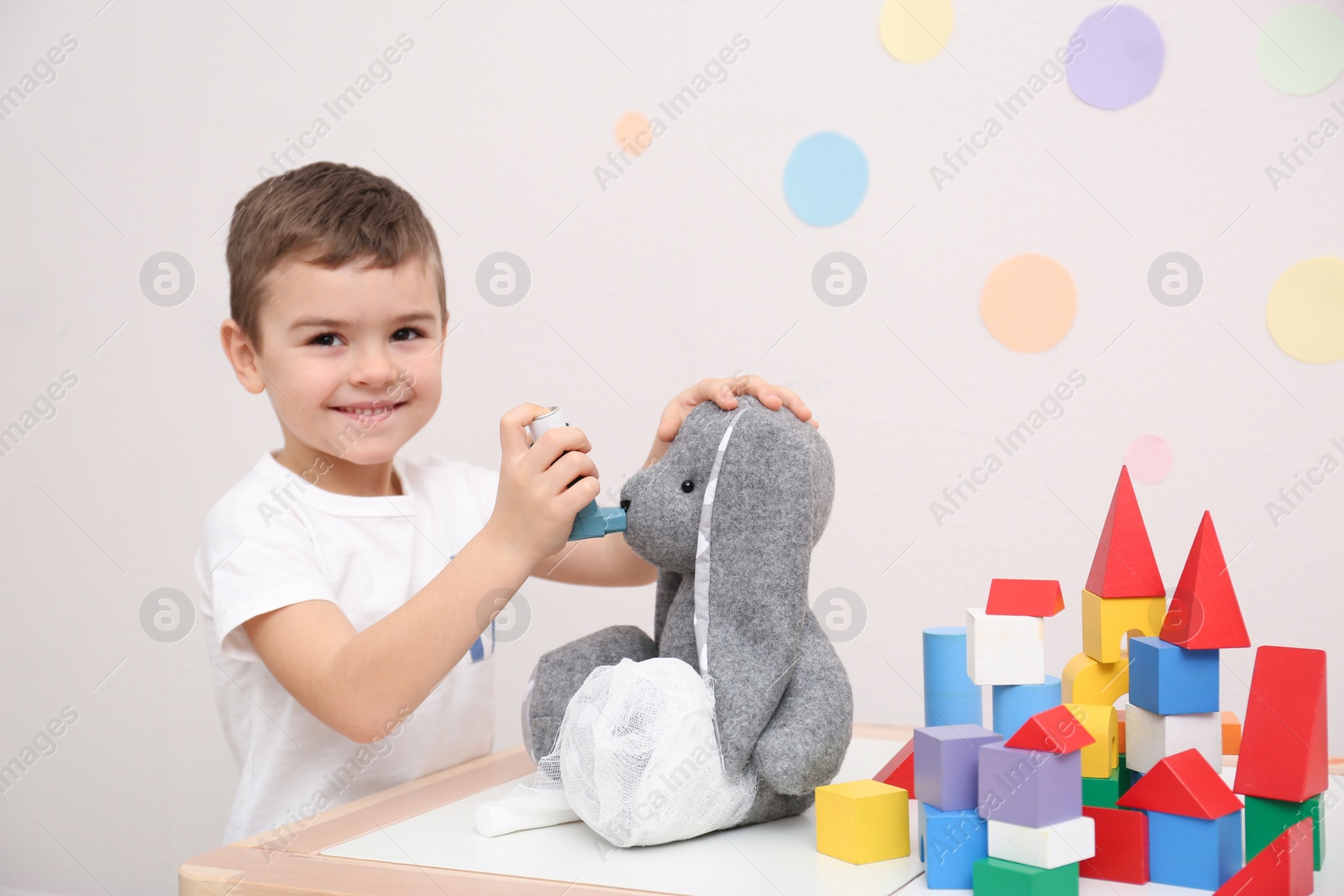 Photo of Cute child playing doctor with stuffed toy at table in hospital