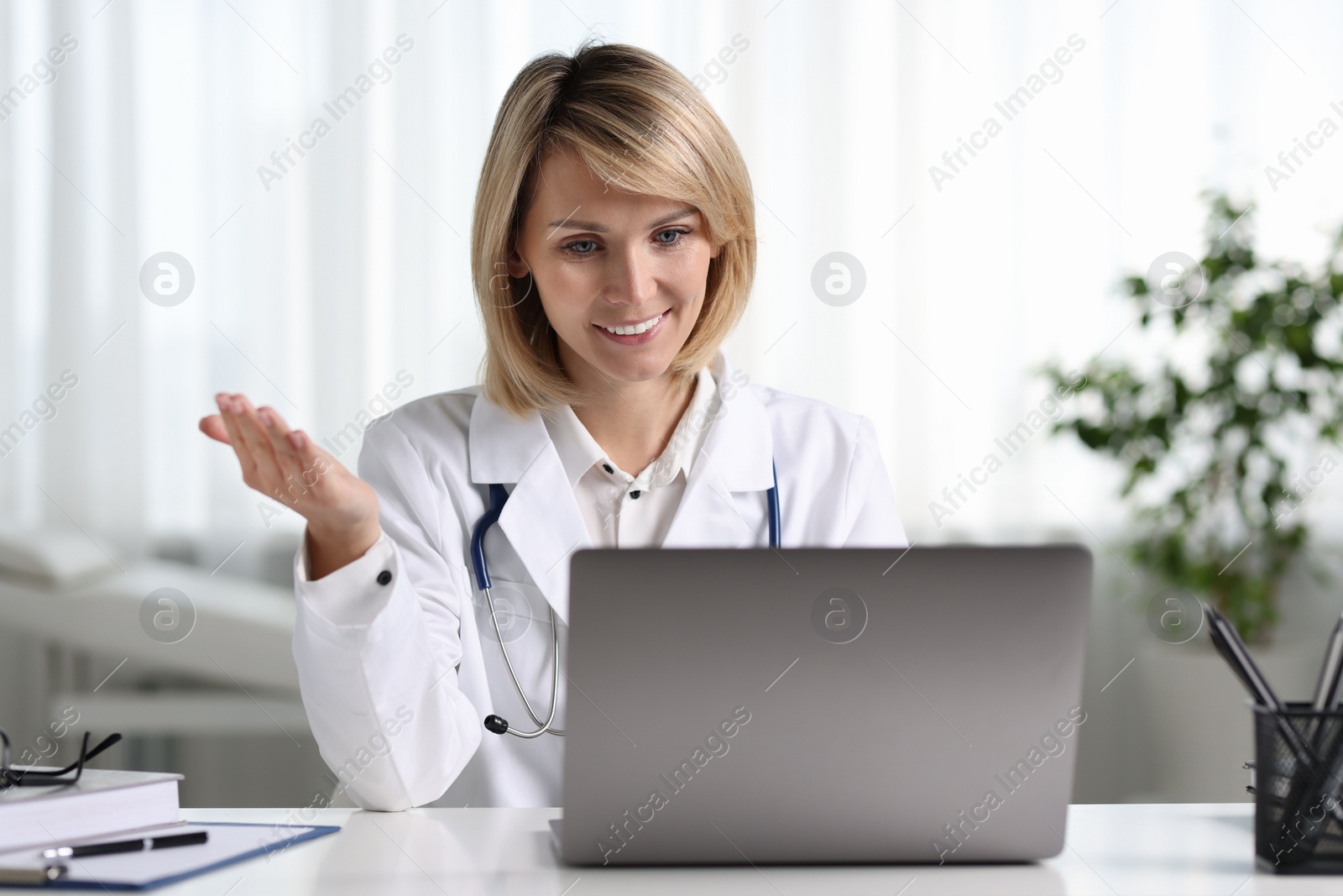 Photo of Smiling doctor with laptop having online consultation at table in office