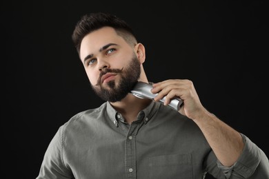 Photo of Handsome young man trimming beard on black background