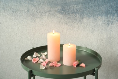 Candles with floral decor on table against color background