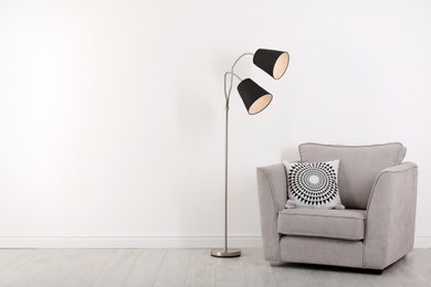 Comfortable armchair and lamp near wall with space for design. Stylish interior elements